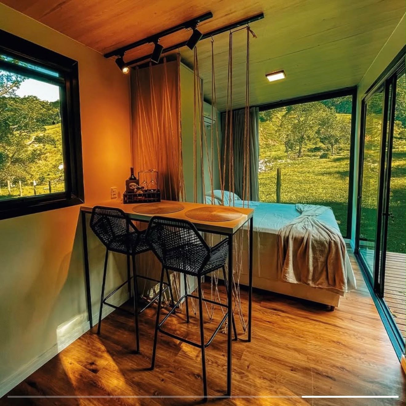 Interior com mesa de bar, cama e janelas para o vale