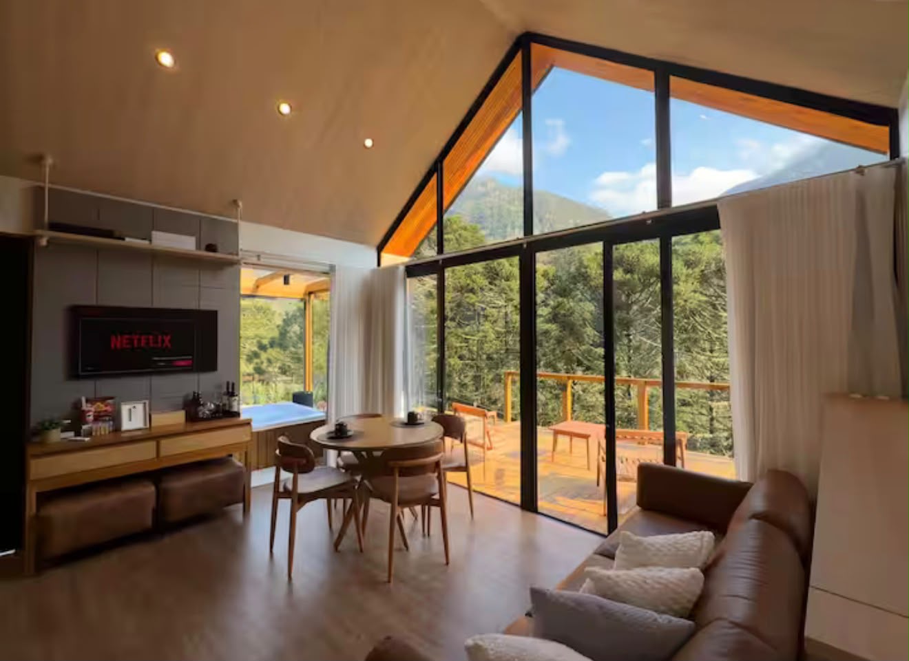 Sala integrada com sofá e fachada envidraçada para a serra