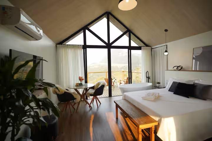 Suíte com pé-direito alto, cama, banheira e janela triangular