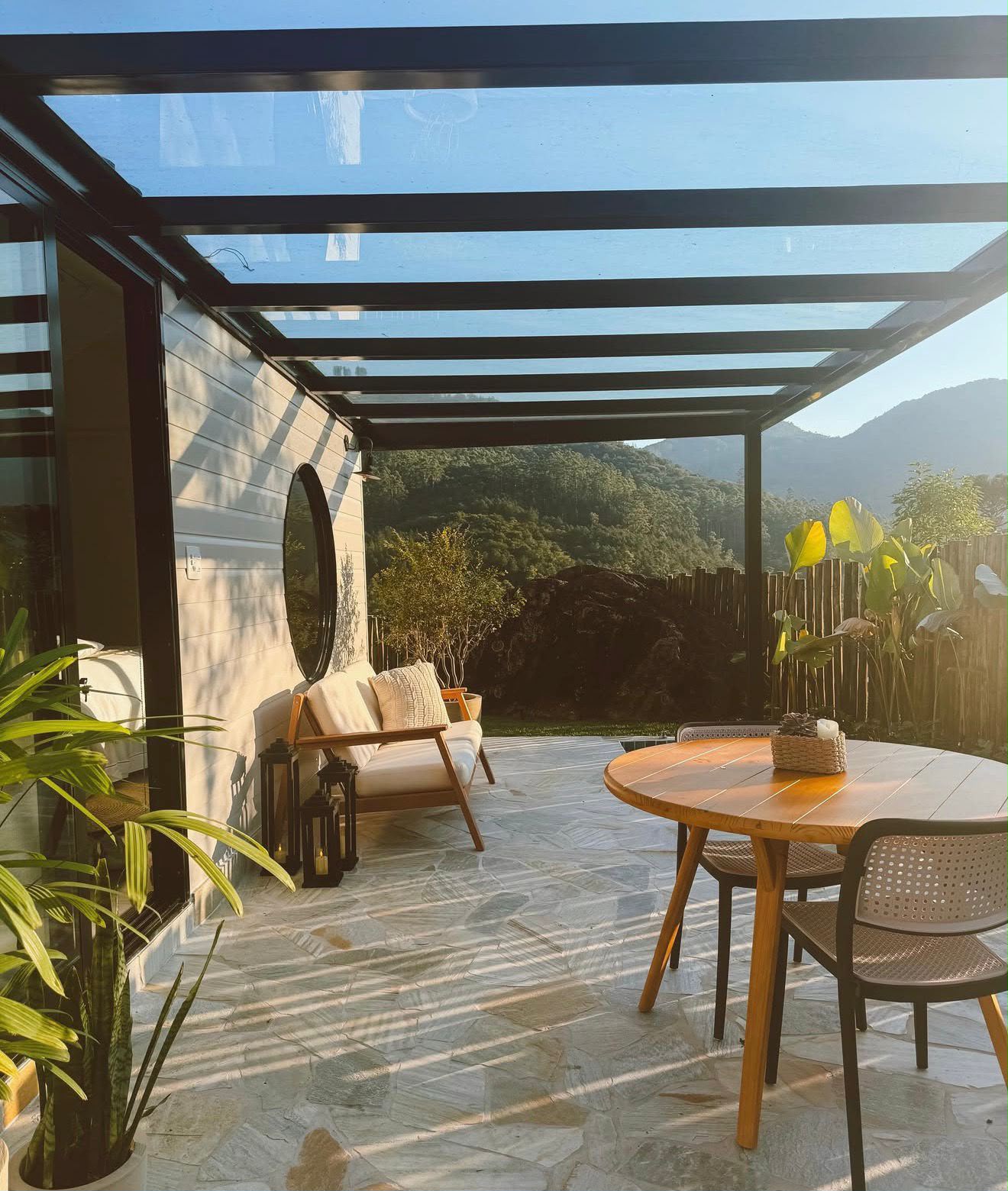 Pérgola de vidro sobre área externa com mesa e poltronas