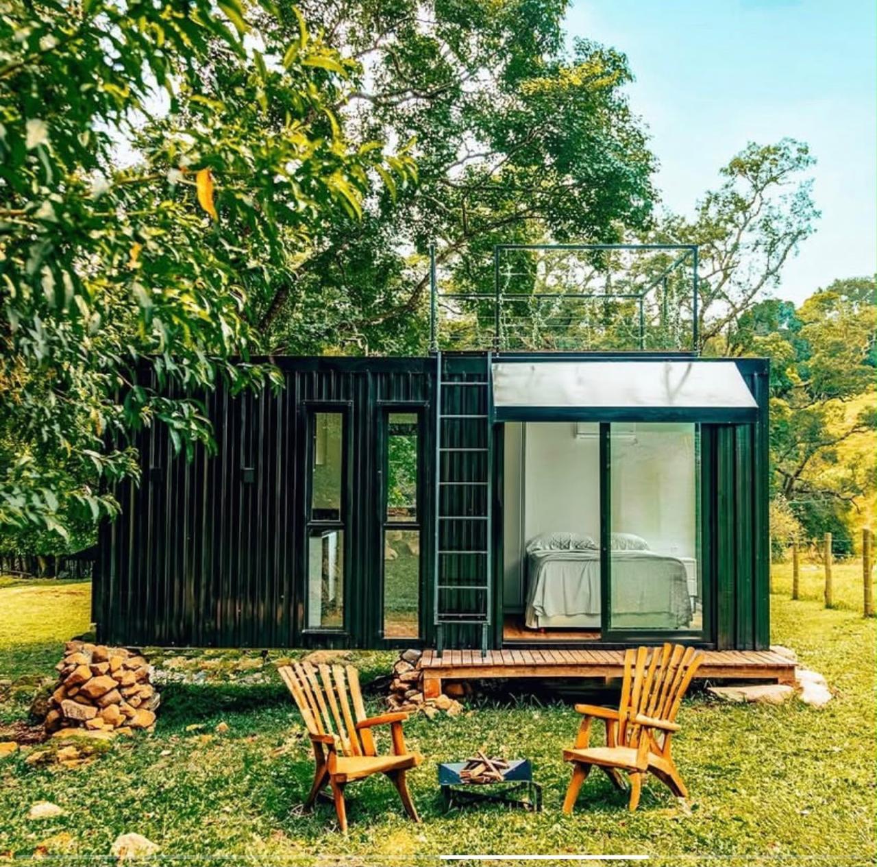 Cabana preta com terraço, poltronas e fogueira no gramado