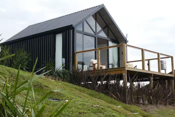 Cabana preta com deck elevado na encosta